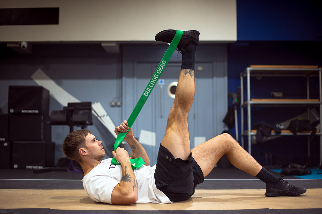 Man using green 20kg Bulldog Gear resistance band to stretch legs